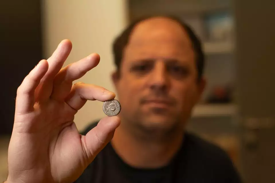 אילן חדד, המפקח על הסחר ברשות העתיקות, עם מטבע השקל הקדום. צילום: יולי שוורץ, רשות העתיקות